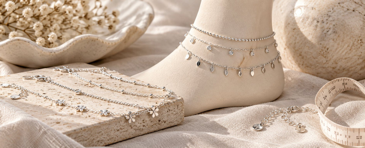Layered silver anklets with charms beside a measuring tape for Jewelry Towns anklet guide