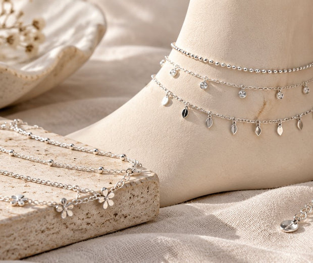 Layered silver anklets with charms beside a measuring tape for Jewelry Towns anklet guide