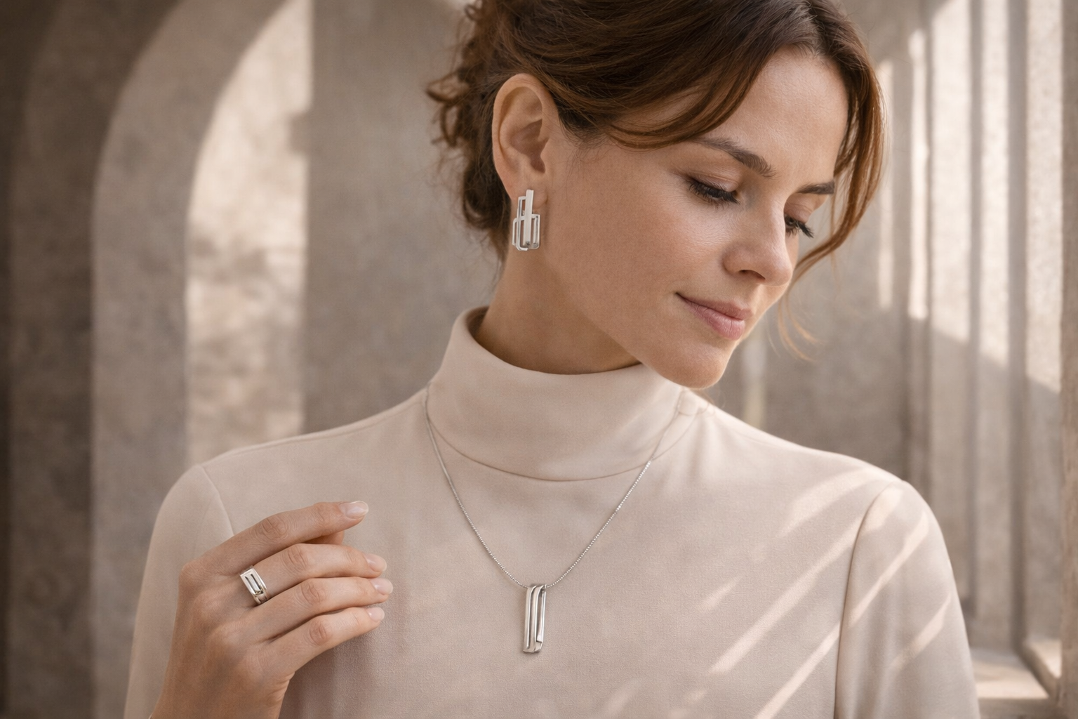 Woman wearing sculptural 925 sterling silver earrings, pendant necklace, and ring in a minimalist architectural setting with soft arch shadows and elegant geometric lines