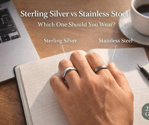 Close-up comparison of a 925 sterling silver ring and stainless steel ring worn on a hand over a workspace desk, illustrating the difference between sterling silver and stainless steel jewelry – 2026 guide