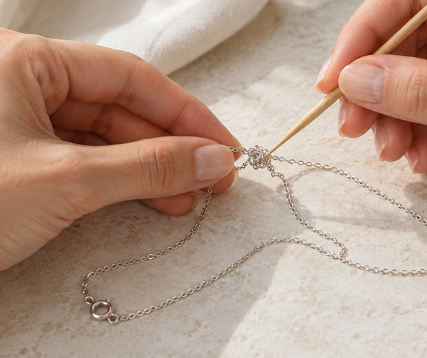 Hands carefully loosening a knot in a fine silver necklace for Jewelry Towns care guide