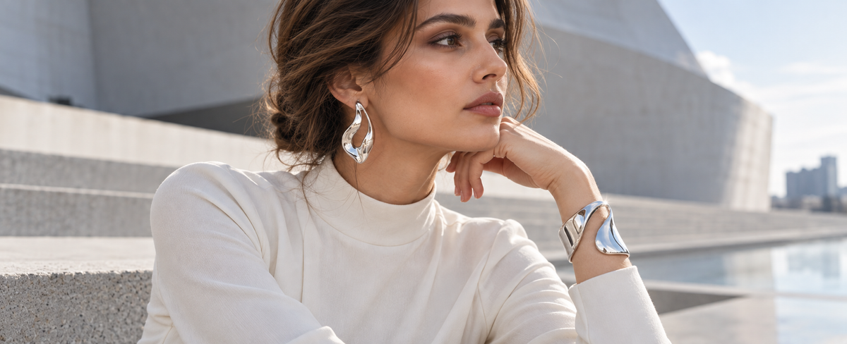 Woman wearing sculptural silver earrings and a polished silver cuff for the 2026 wearable art jewelry trend